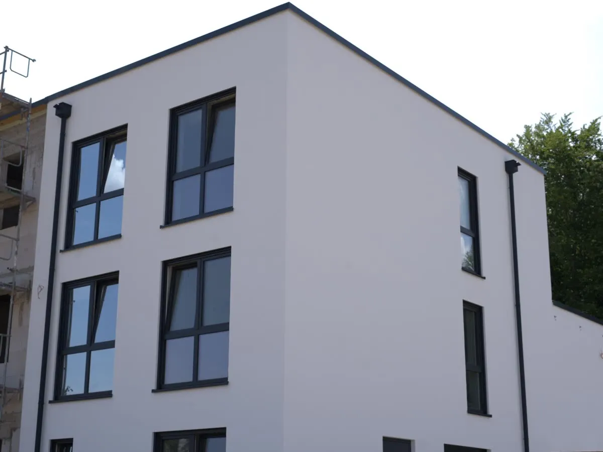 Mehrgeschossiger Neubau: Anthrazitfenster, teils mit Sprossenkreuz, auf weißem Putz.